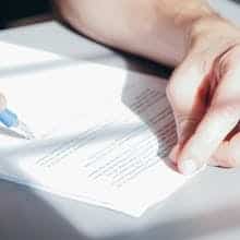 Hands signing with a blue pen, close-up view by Kindel Media