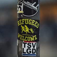 Photo: Street pole with stickers including 'Refugees Welcome', a message of acceptance and solidarity. Credit: Markus Spiske