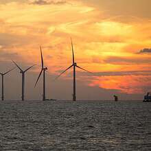 A serene view of wind turbines silhouetted against a vibrant sunset over the sea, showcasing renewable energy.