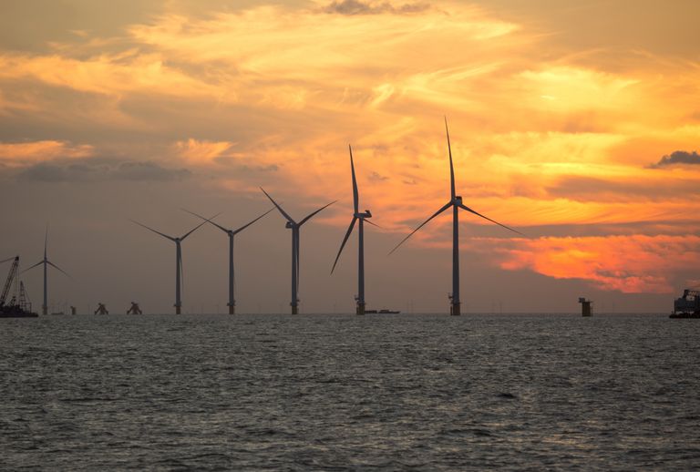 A serene view of wind turbines silhouetted against a vibrant sunset over the sea, showcasing renewable energy.