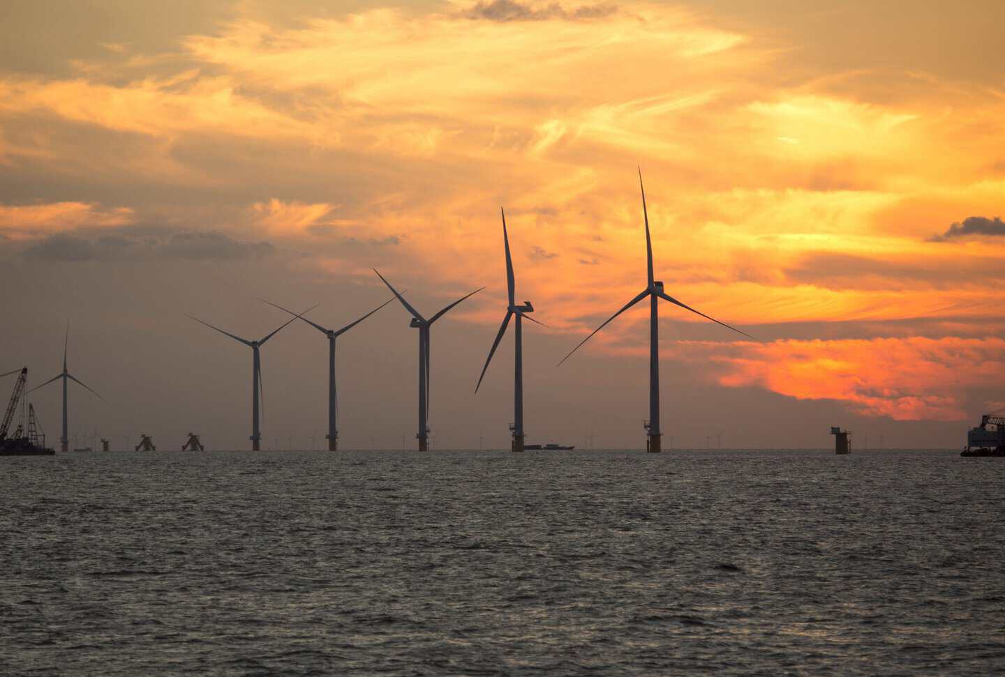A serene view of wind turbines silhouetted against a vibrant sunset over the sea, showcasing renewable energy.